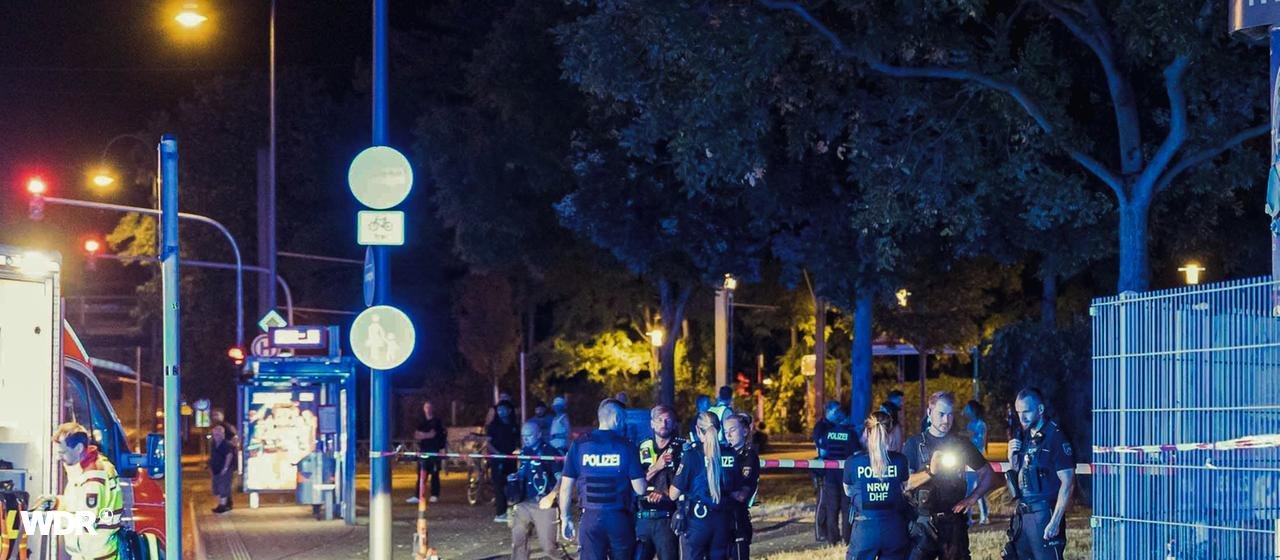 Polizeieinsatz nach Schüssen in Köln-Mülheim | dpa / Daniel Evers Polizisten vor und hinter einer Absperrung auf einer Kölner Straße